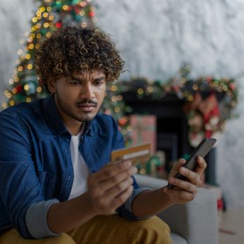 A man holding a smartphone in his left hand and a gift card in his right hand, looking concerned