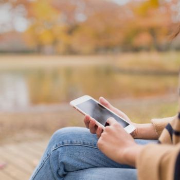 Consumer viewing a smartphone while sitting beside a pond during autumn