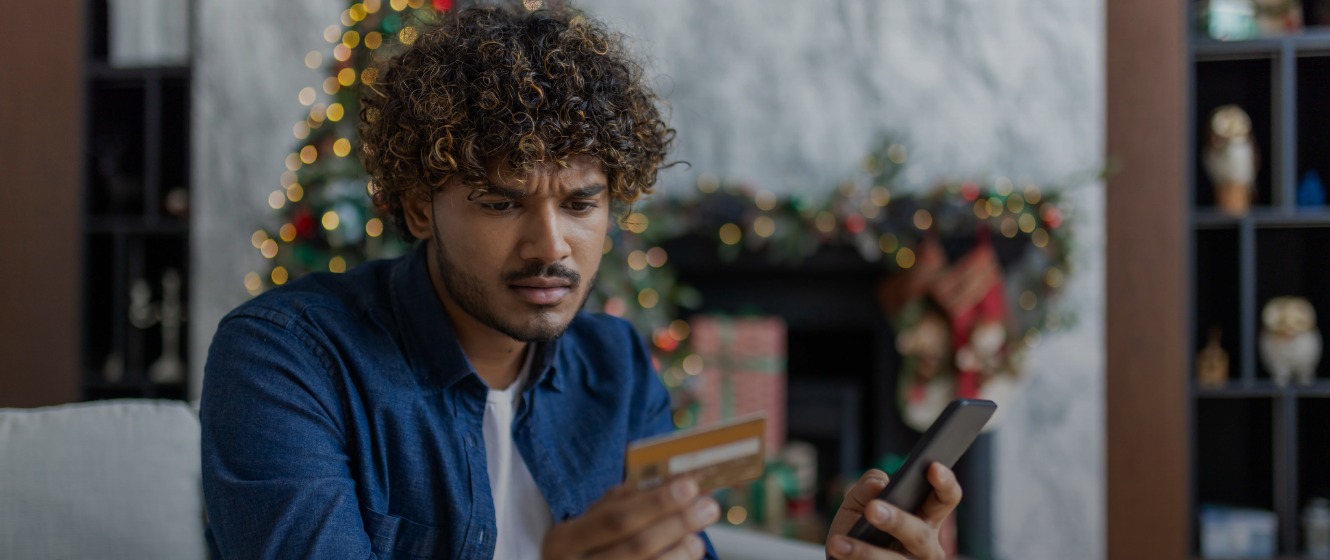 A man holding a smartphone in his left hand and a gift card in his right hand, looking concerned