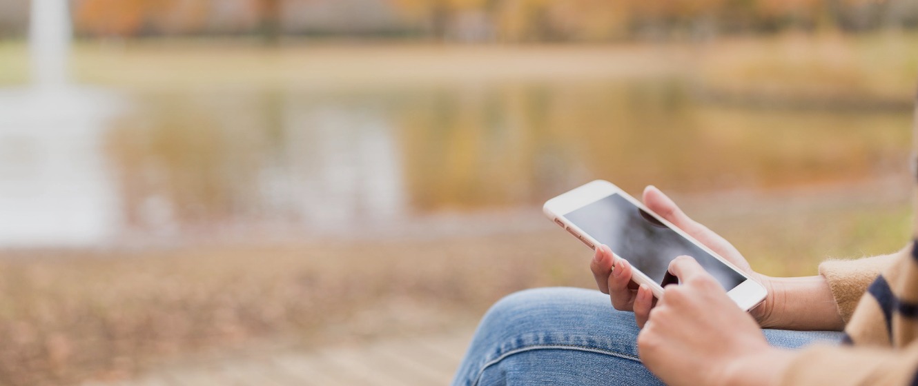 Consumer viewing a smartphone while sitting beside a pond during autumn