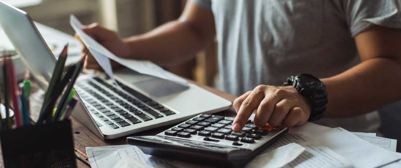 Person at desk with laptop open and working on calculator for bills