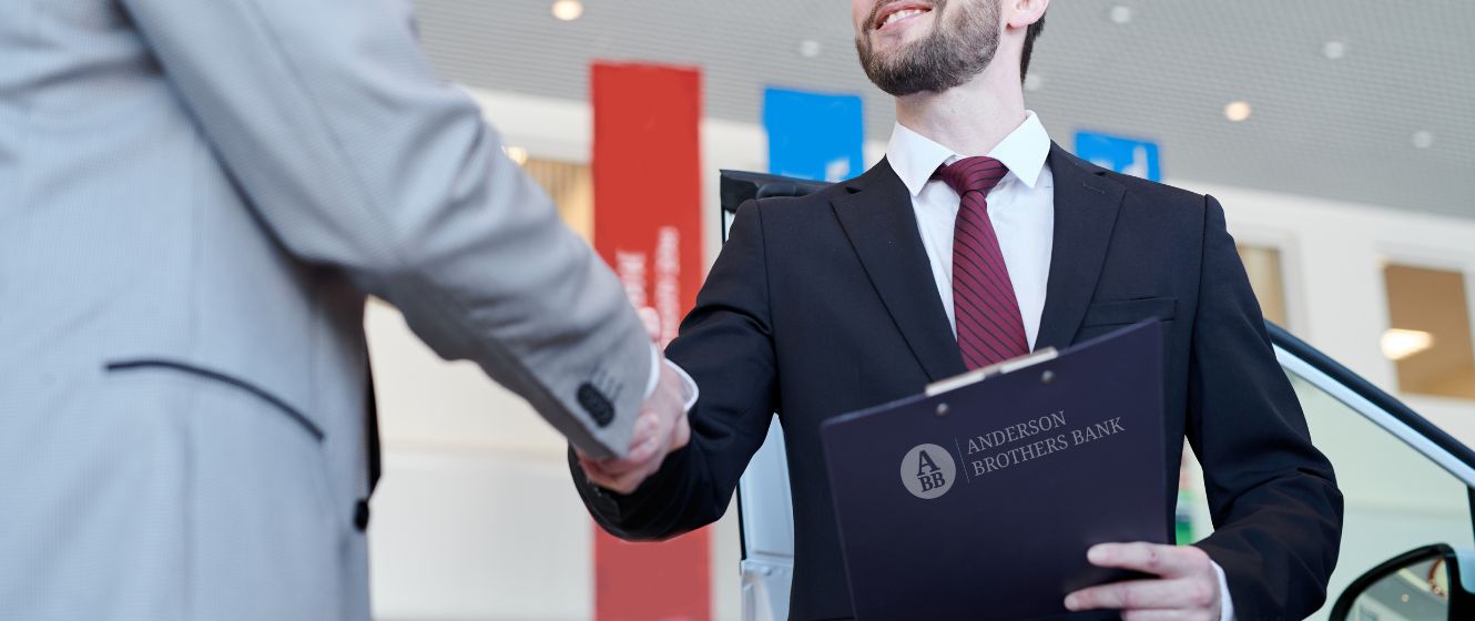 Closing a deal, two people shaking hands while one is holding an Anderson Brothers Bank clipboard