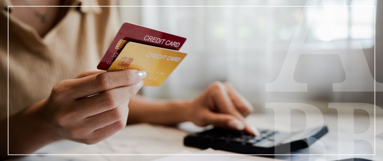 A woman holding credit cards is comparing while using a calculator